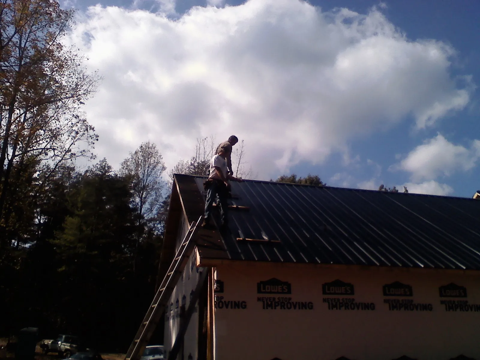 Roofer fastening dark metal panels high against a cloudy sky, from a Roof Inspection job in South Salem
